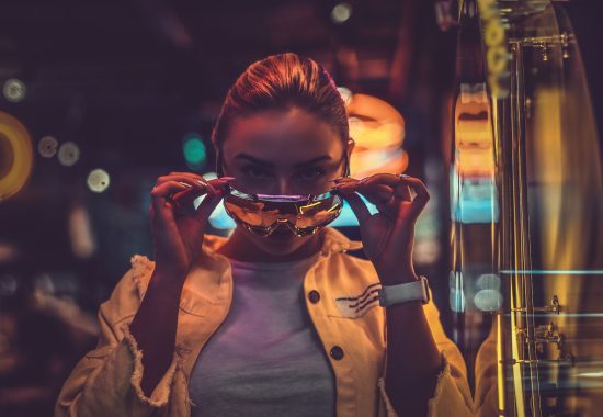 Beautiful pensive trendy girl is posing for photographer in neon lights. There are darkness at background.