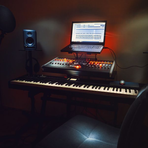 Interior of a small bedroom recording studio, details of equipment, microphone in foreground and modern mixing console with laptop in background.
